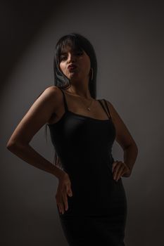 A stylish woman in a black dress strikes a confident pose against a dark background.
