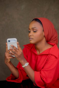 A woman in a red hijab is focused on her smartphone, engaging with technology.