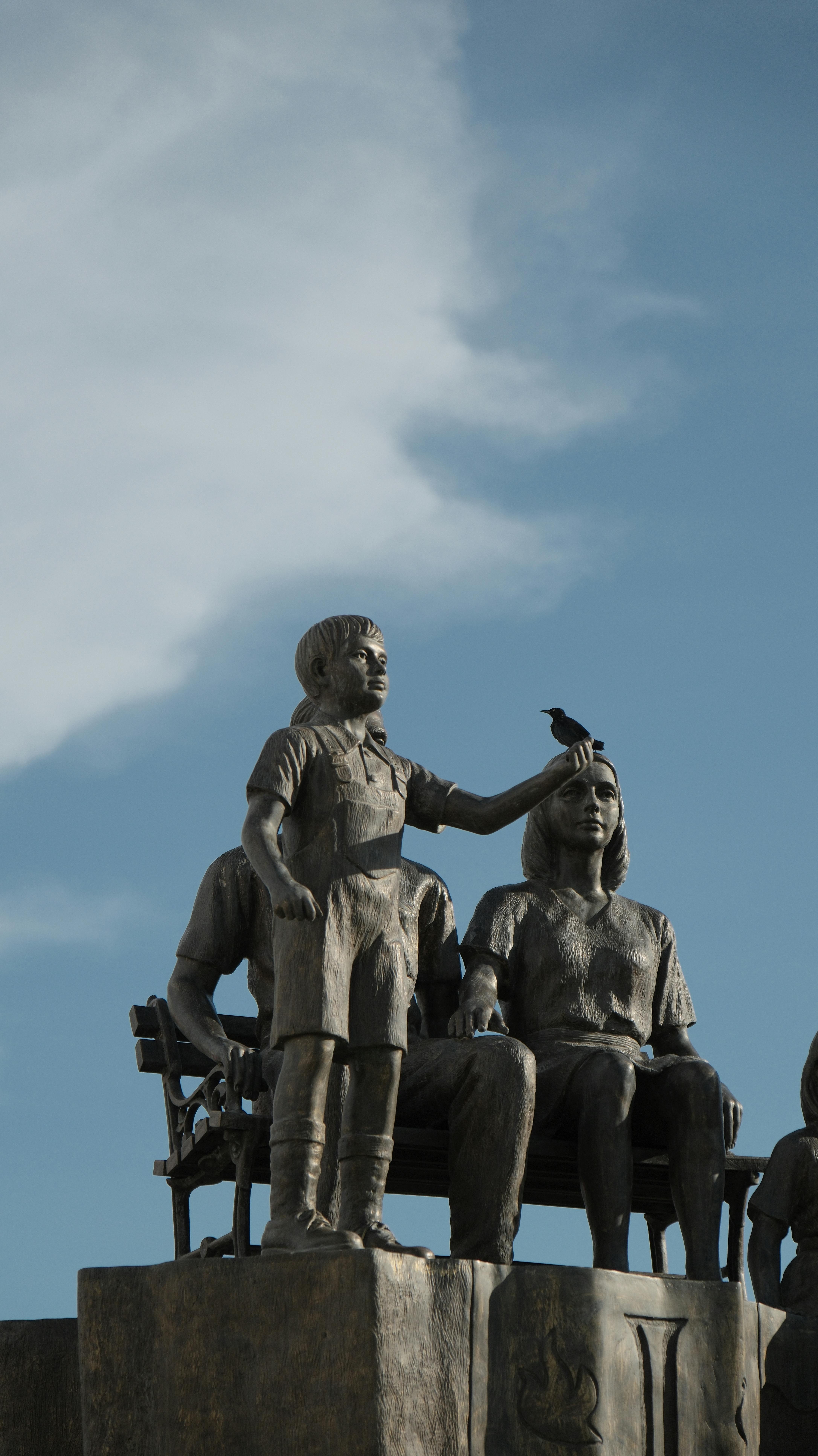 A captivating statue depicting a child with a bird on their head, set against a blue sky.