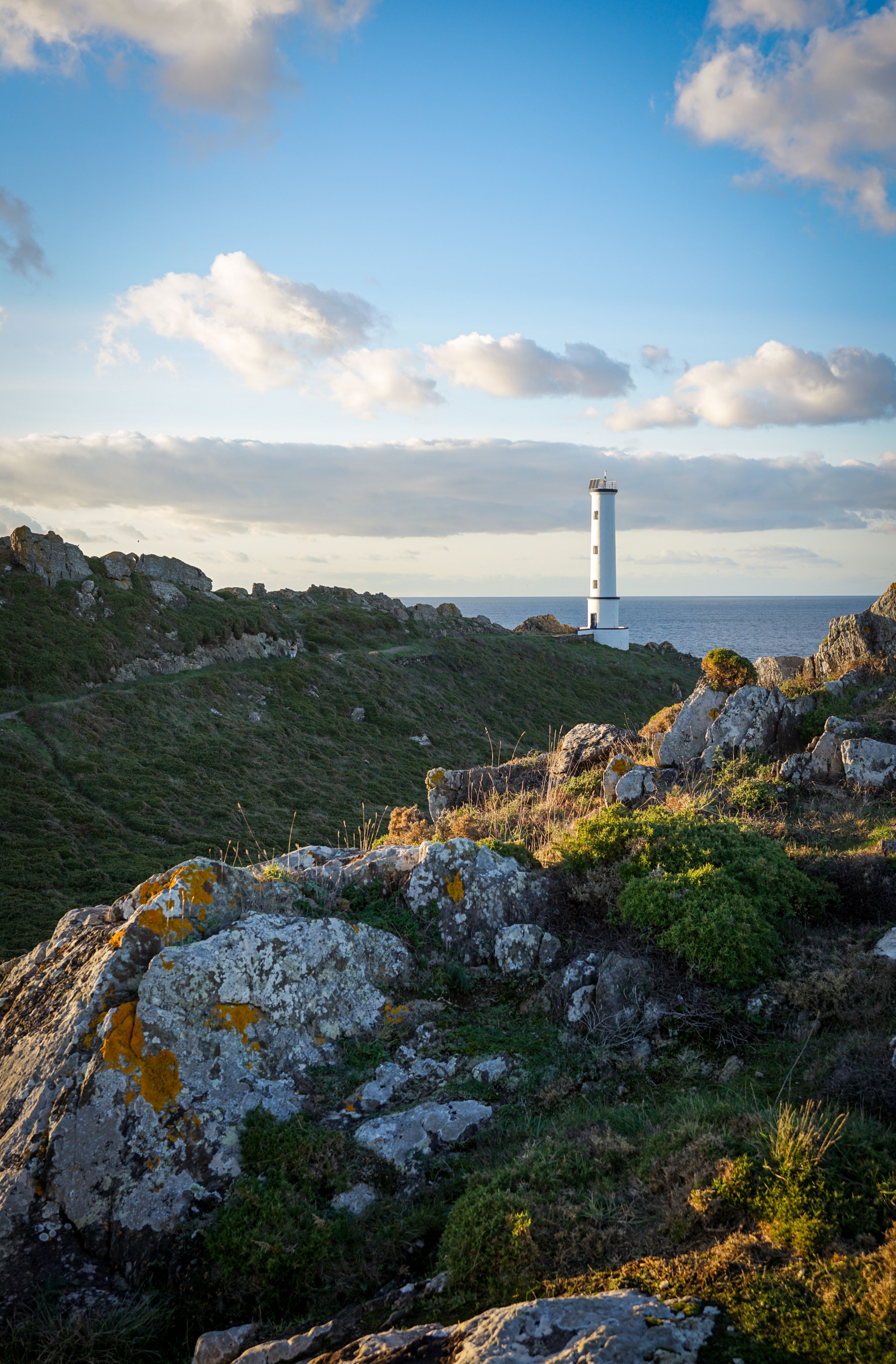 A beautiful view of a lighthouse on a rocky coastline with a dramatic sky at sunset.