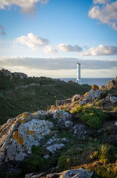A beautiful view of a lighthouse on a rocky coastline with a dramatic sky at sunset.
