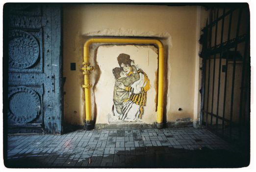 Street art mural framed by industrial pipes and a rustic gate indoors.