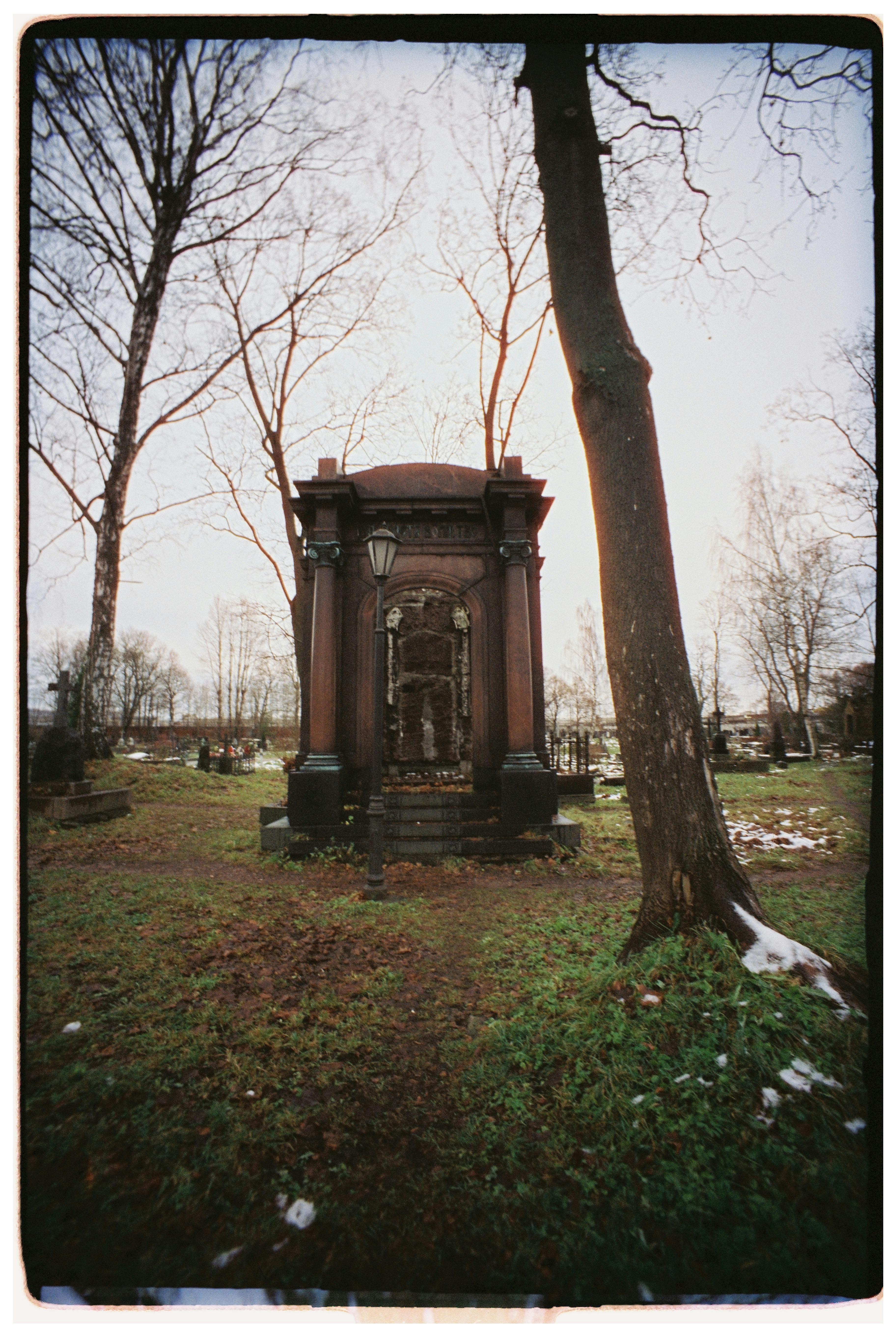Historic mausoleum amidst bare trees and green grass in a tranquil cemetery setting.
