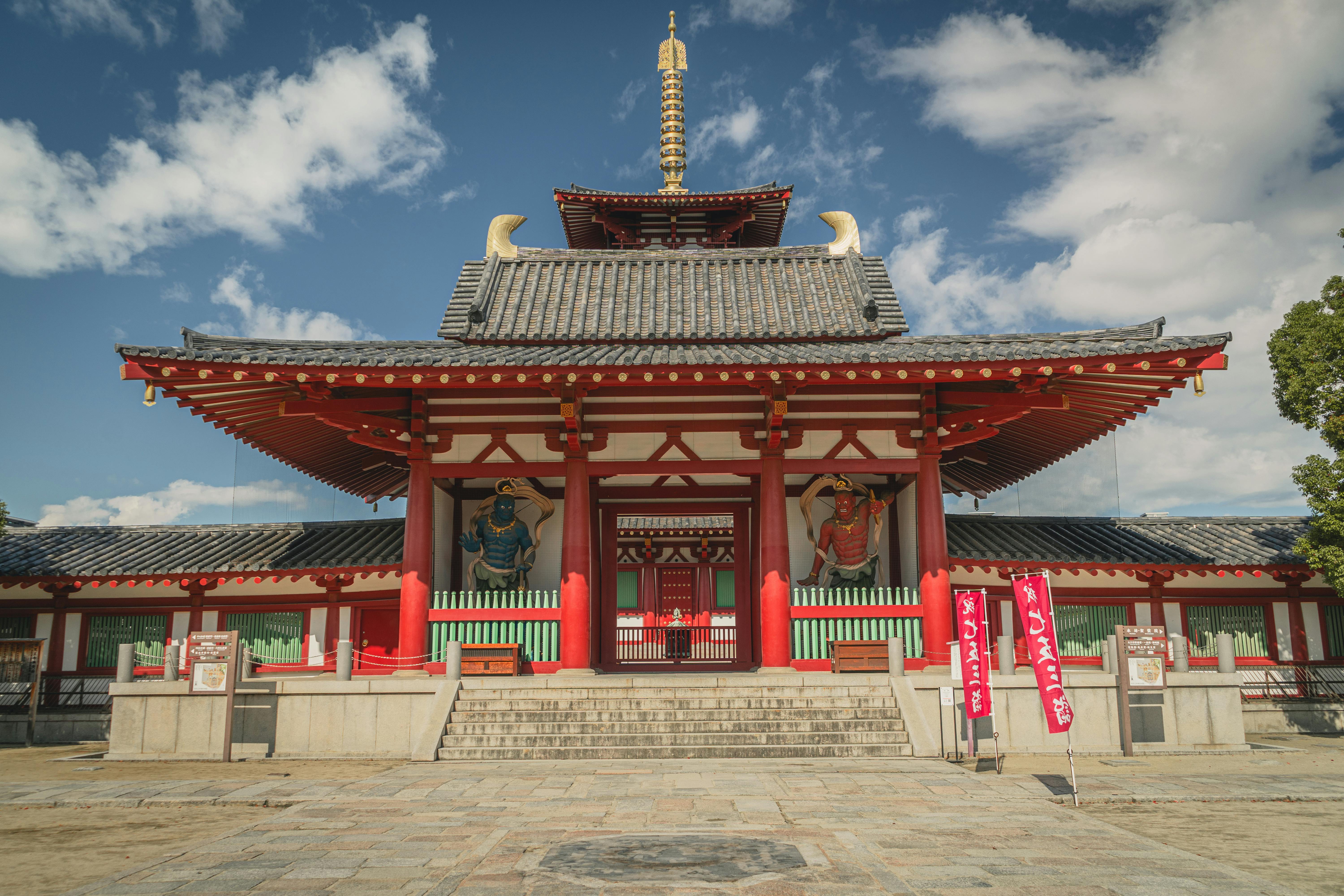 Front view of Shitennoji Temple with vibrant red architecture in Osaka, Japan, under a clear sky.