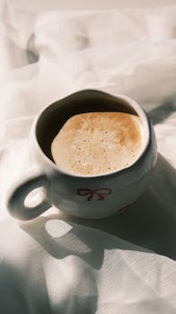 Warm cup of frothy coffee in a decorative mug on soft fabric, capturing tranquility.