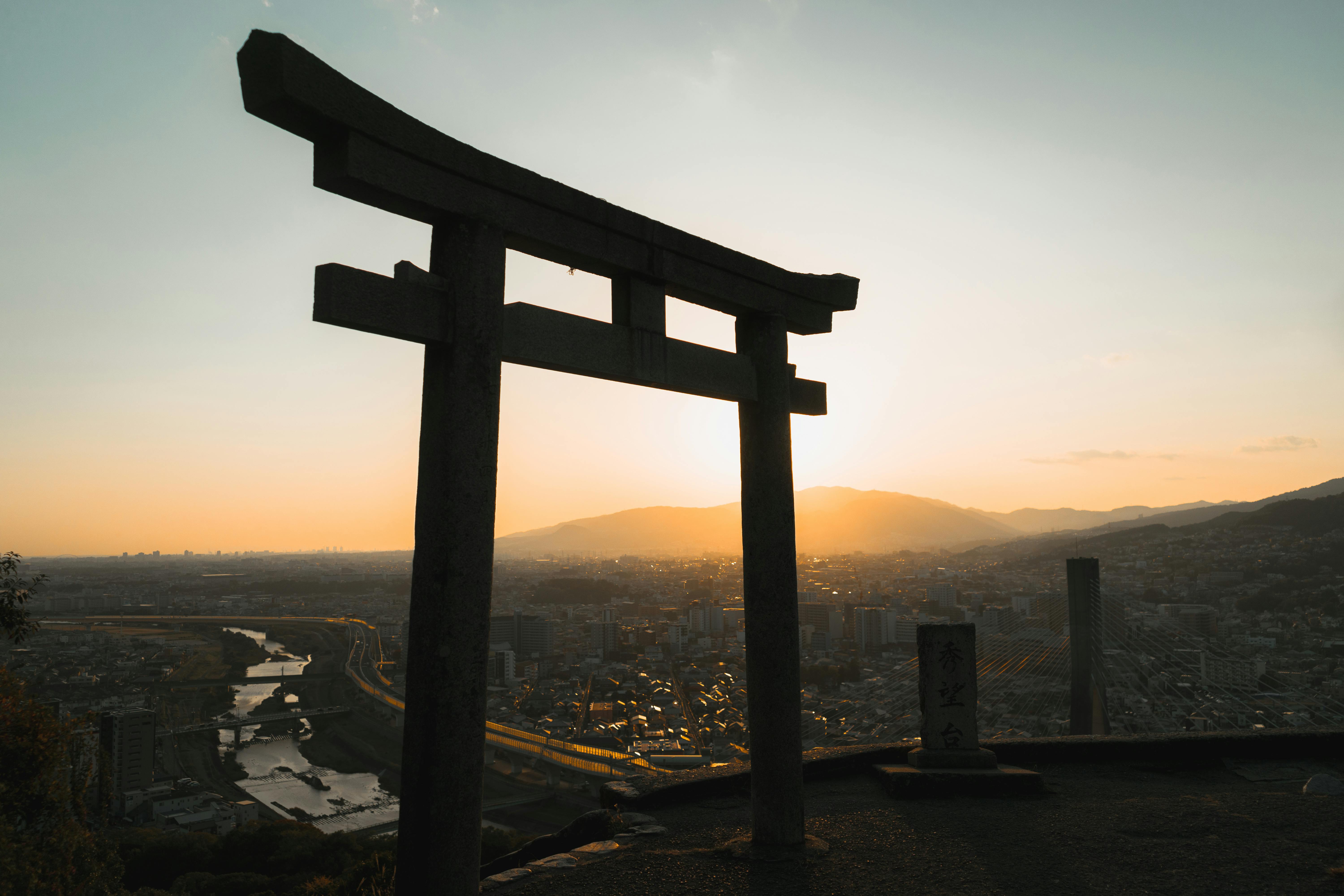 Sunset view of Torii gate overlooking Ikeda cityscape in Osaka, Japan, creating a serene silhouette.