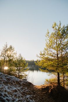 A tranquil winter scene with pine trees and a peaceful lake reflecting the morning sun.