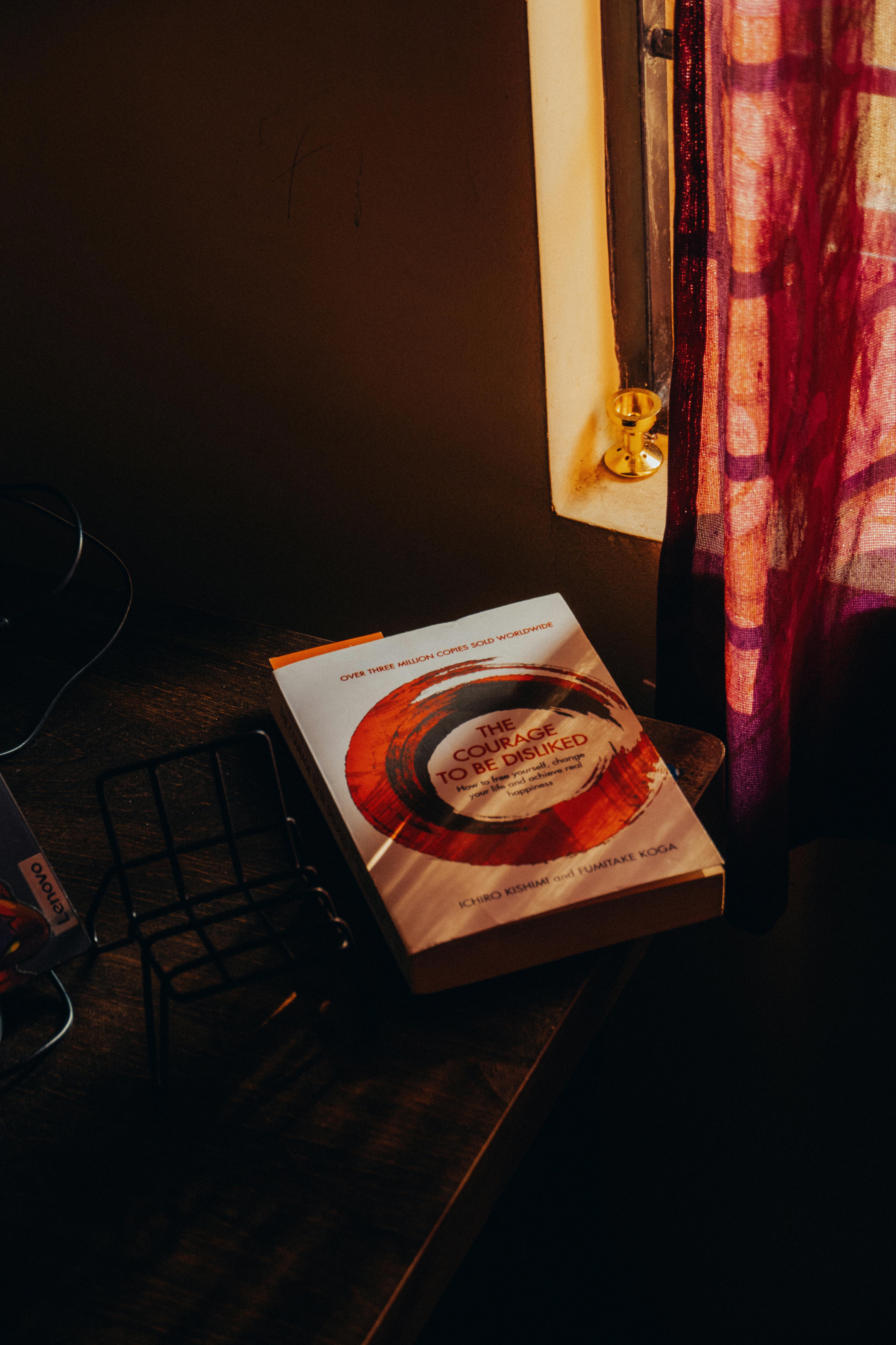 bezplatná Útulný koutek s otevřenou knihou zalitou teplým slunečním světlem na pozadí slabě osvětleného interiéru. Základová fotografie