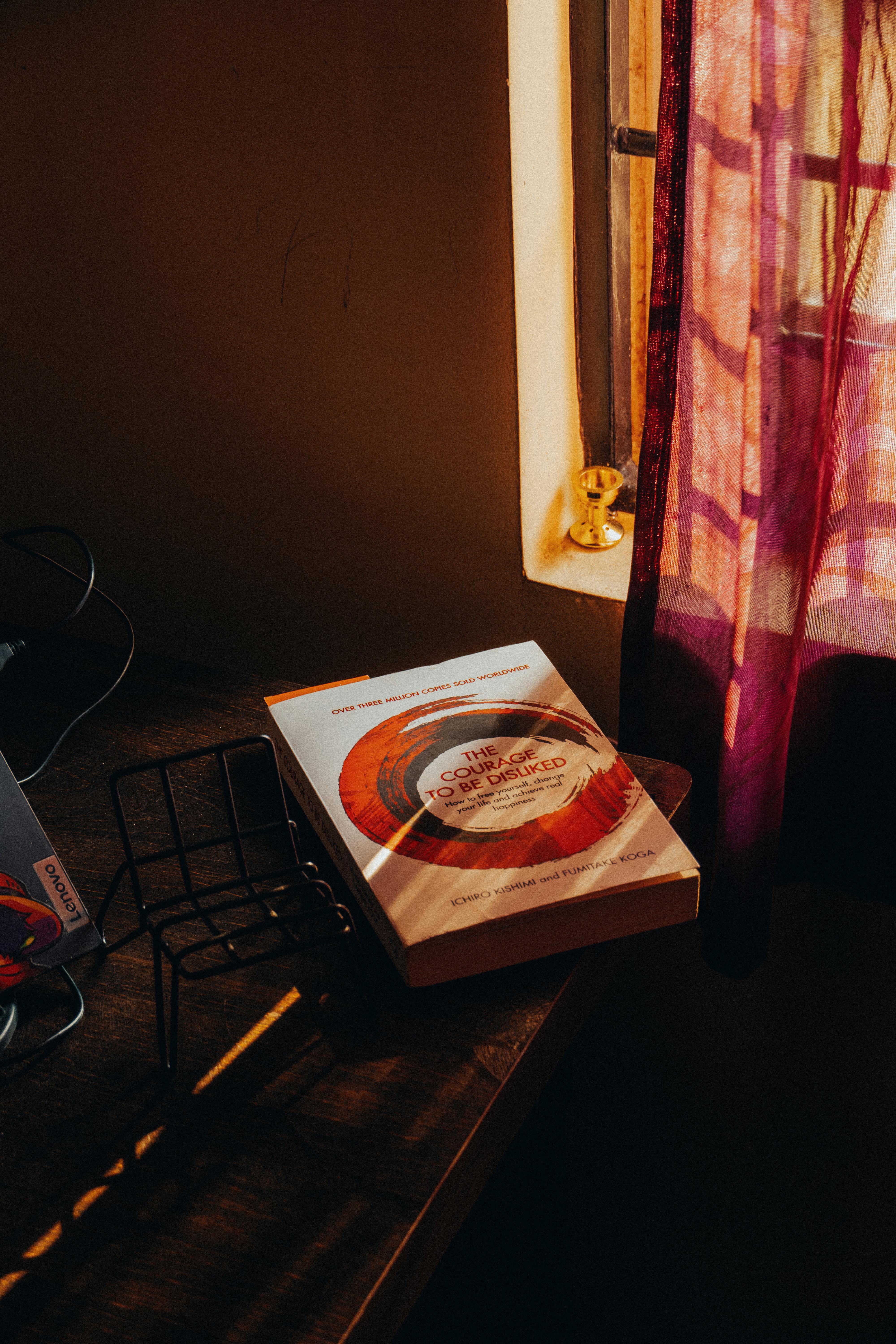 De franc Una escena interior tranquil·la amb un llibre a la finestra, banyada per la càlida llum del sol de la tarda. Foto d'estoc