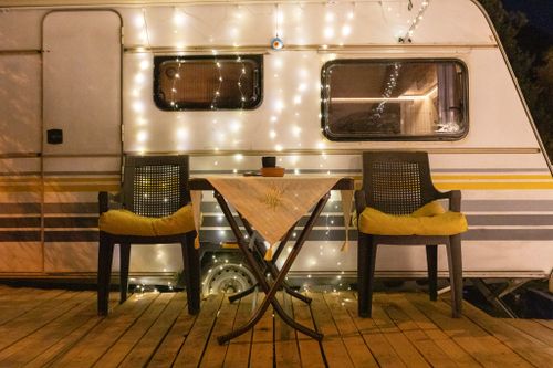 Free A warmly lit camper van setup with chairs and fairy lights, perfect for a relaxing night outdoors. Stock Photo