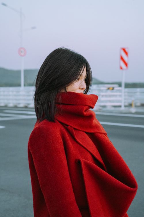 Free Woman in stylish red coat stands on a city street, exuding modern fashion. Stock Photo