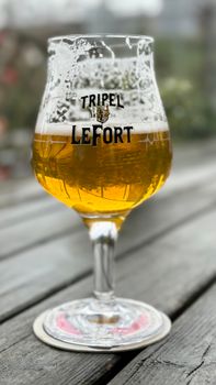 Tripel Lefort beer in a glass on a wooden table, outdoors.