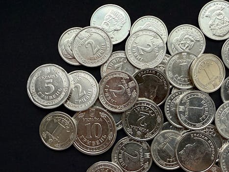 Pile of Ukrainian Hryvnia coins scattered on a dark background, showcasing different denominations.