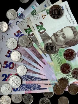 A collection of Ukrainian hryvnia banknotes and coins displaying different denominations laid out against a black background.