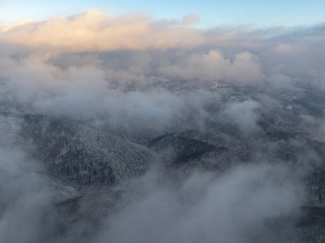 A breathtaking aerial view showcasing snow-covered mountains amidst fluffy clouds at sunrise.