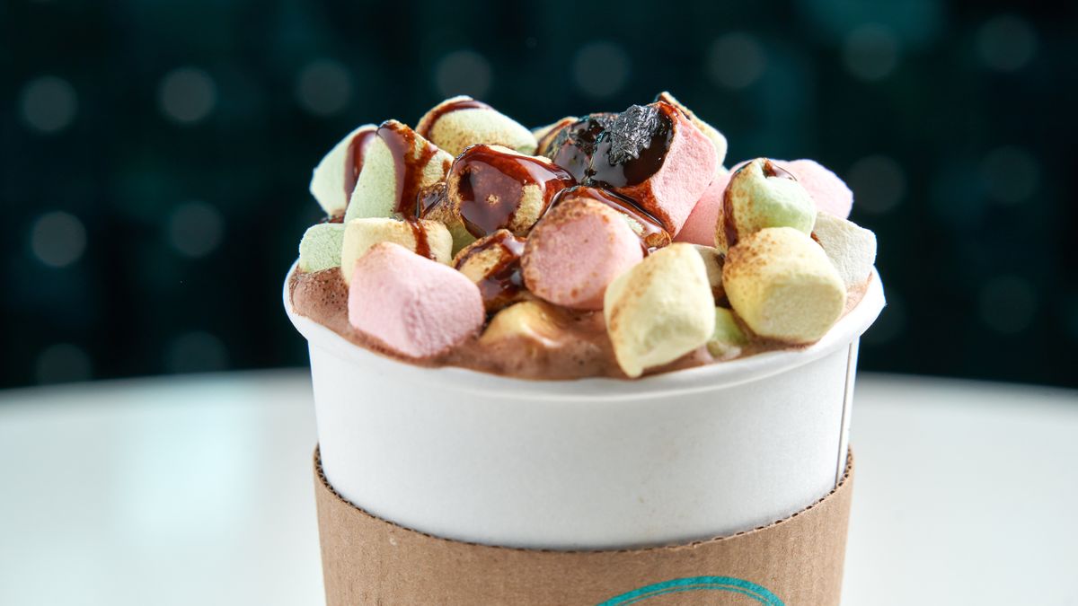 Close-up of hot chocolate topped with colorful marshmallows and chocolate syrup in a to-go cup.
