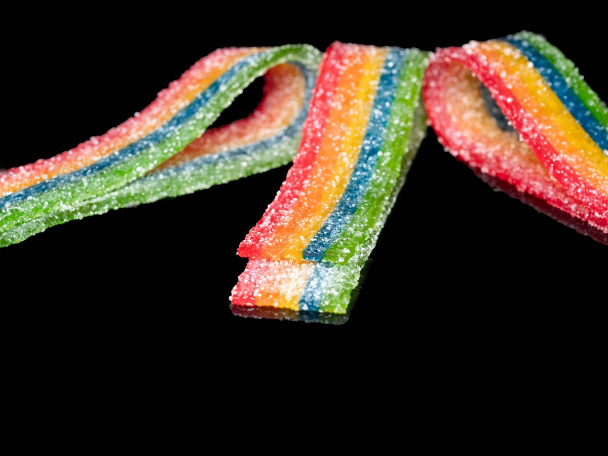 Vibrant rainbow-colored candy strips with sugar crystals against a black background, highlighting their vivid hues.