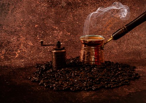Free Aromatic Turkish coffee brewing in a cezve with steam rising, surrounded by roasted coffee beans and a vintage grinder. Stock Photo