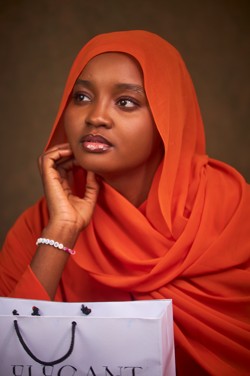 Free Portrait of a woman in a vibrant orange hijab looking contemplative indoors. Stock Photo