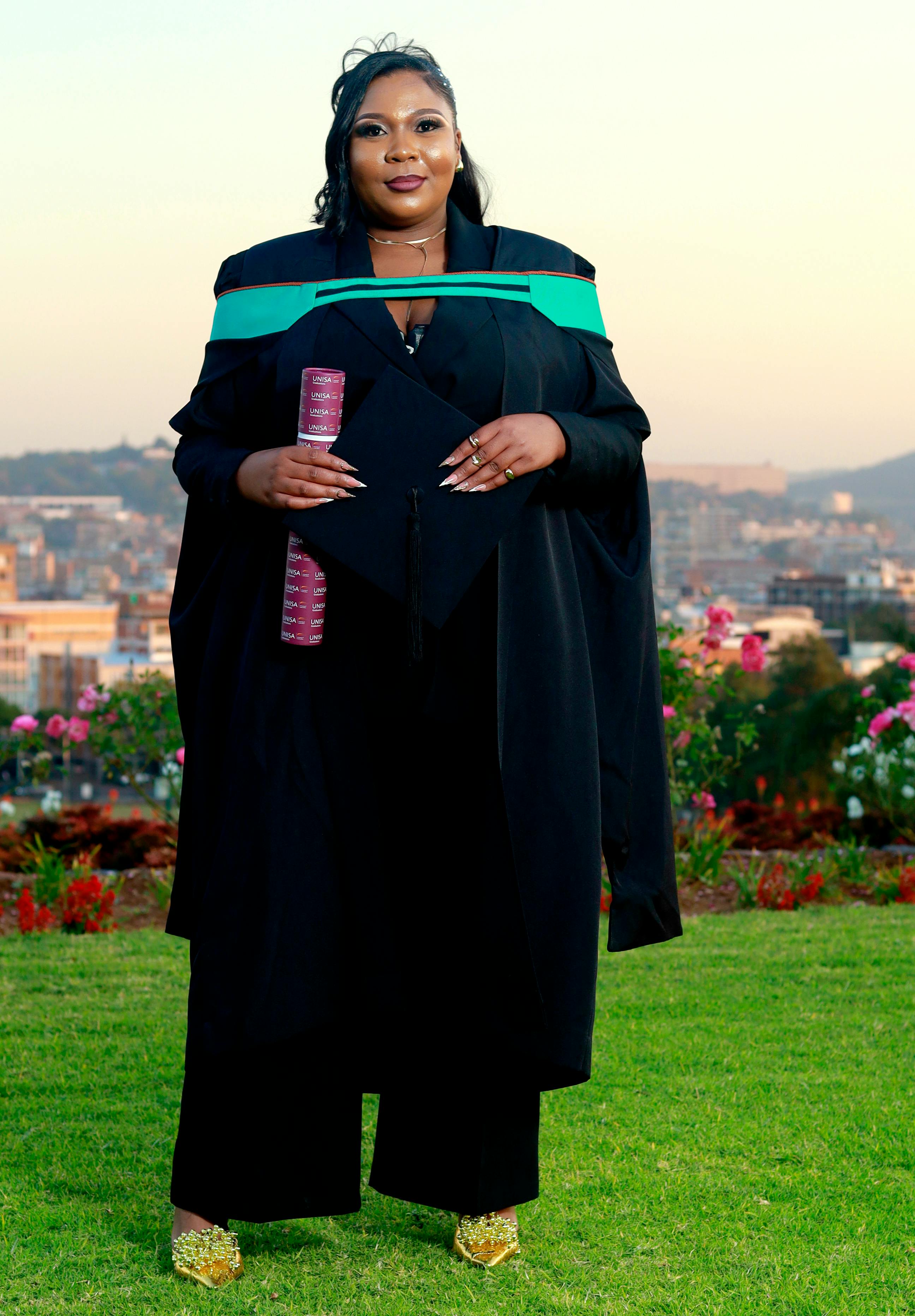 Female graduate in cap and gown holding diploma with scenic city view outdoor.
