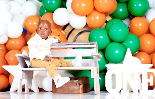 Baby boy on bench in front of vibrant balloons during first birthday celebration.