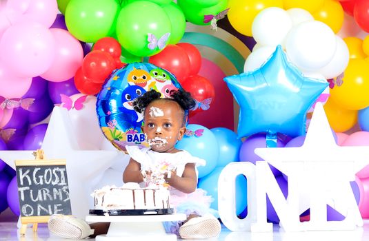 Adorable first birthday party setup with colorful balloons and a cute baby enjoying cake.
