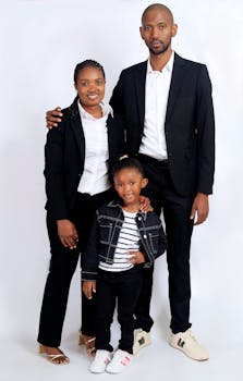 A cheerful family of three posing in matching formal outfits against a white background.