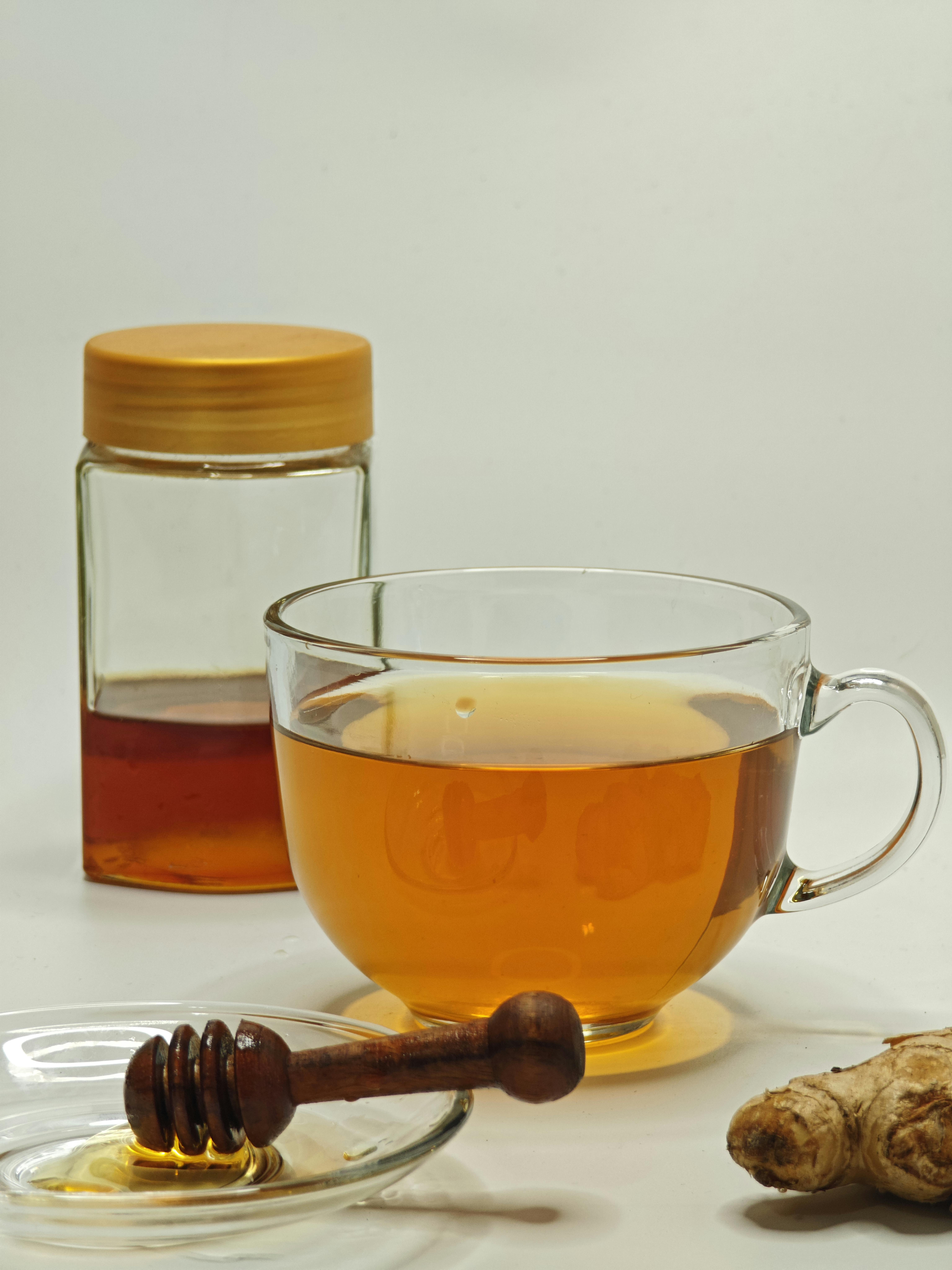 Glass cup of ginger tea with honey jar and ginger root, perfect for a cozy drink.