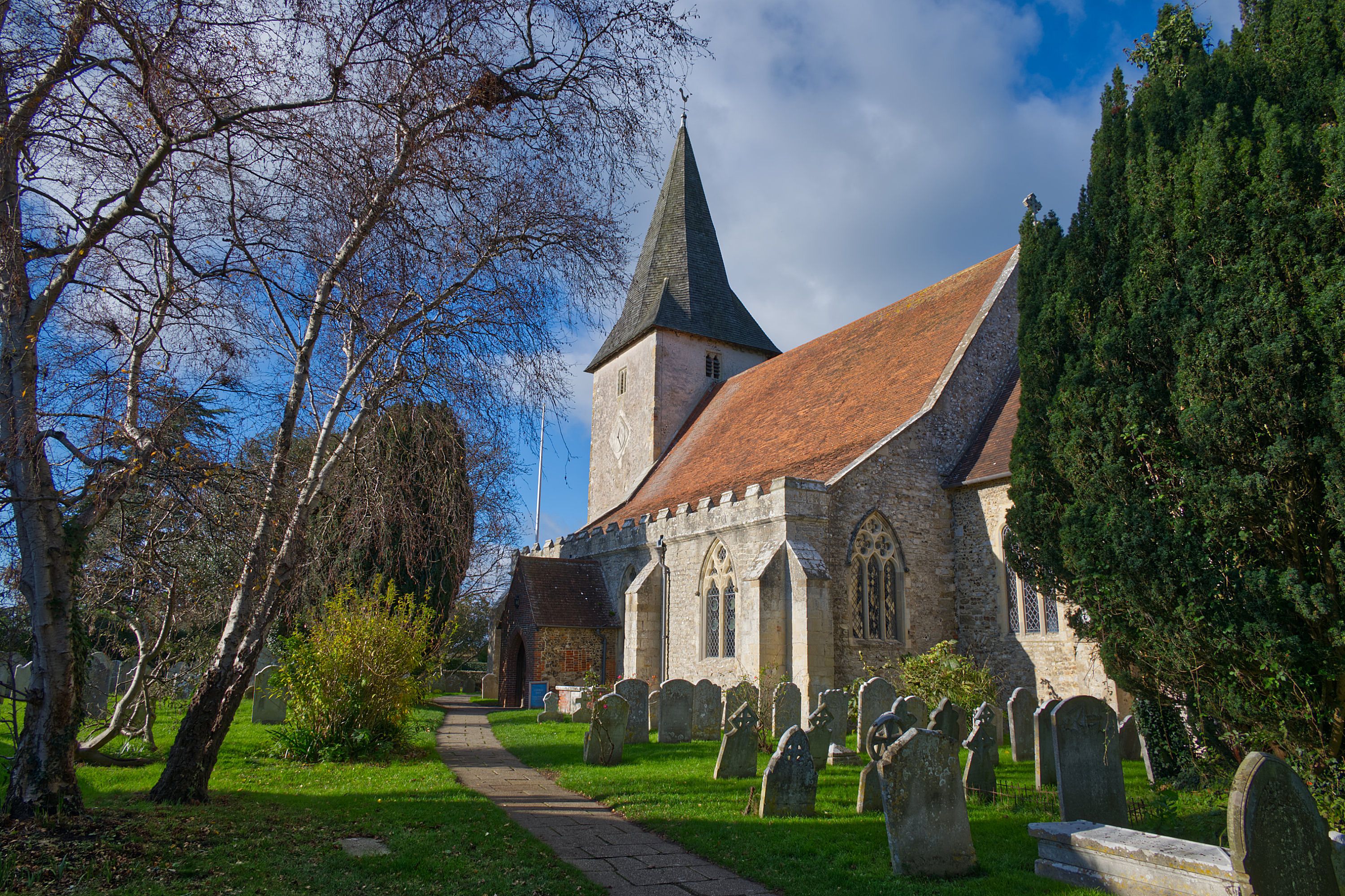 Charming Bosham church with graveyard on a sunny day, surrounded by trees.