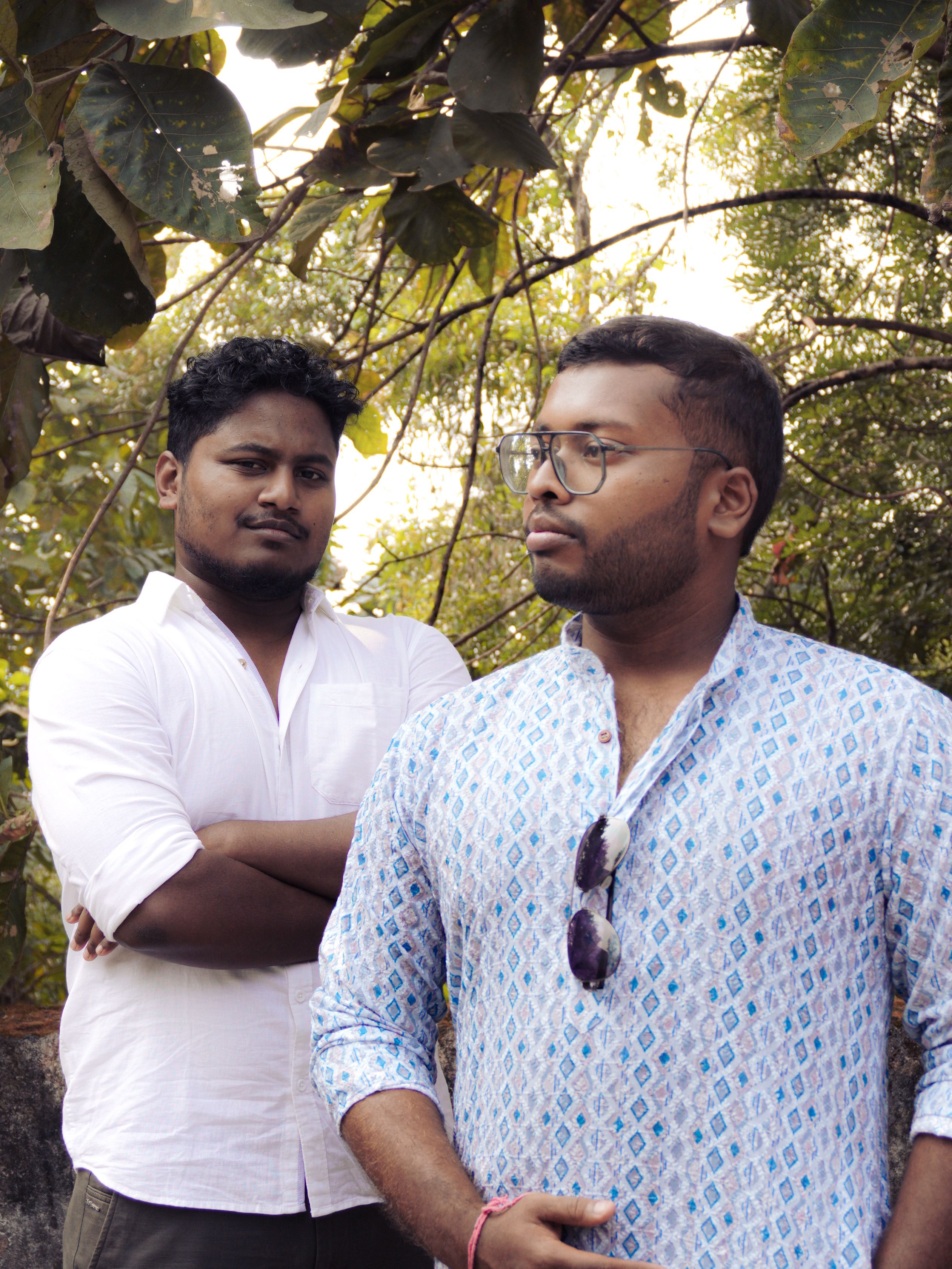 Two men dressed in casual clothes posing in a natural outdoor setting.