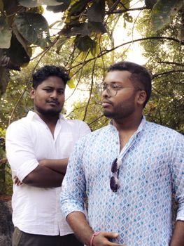 Two men dressed in casual clothes posing in a natural outdoor setting.