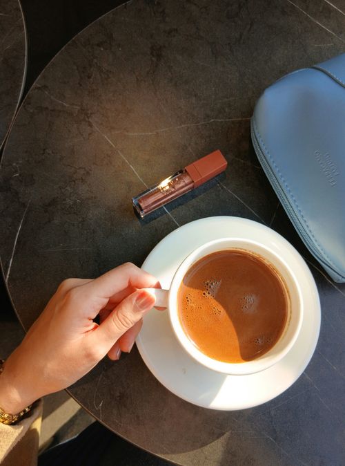 Free A sophisticated coffee setup with a hand lifting the cup, lipstick, and purse on a marble table. Stock Photo