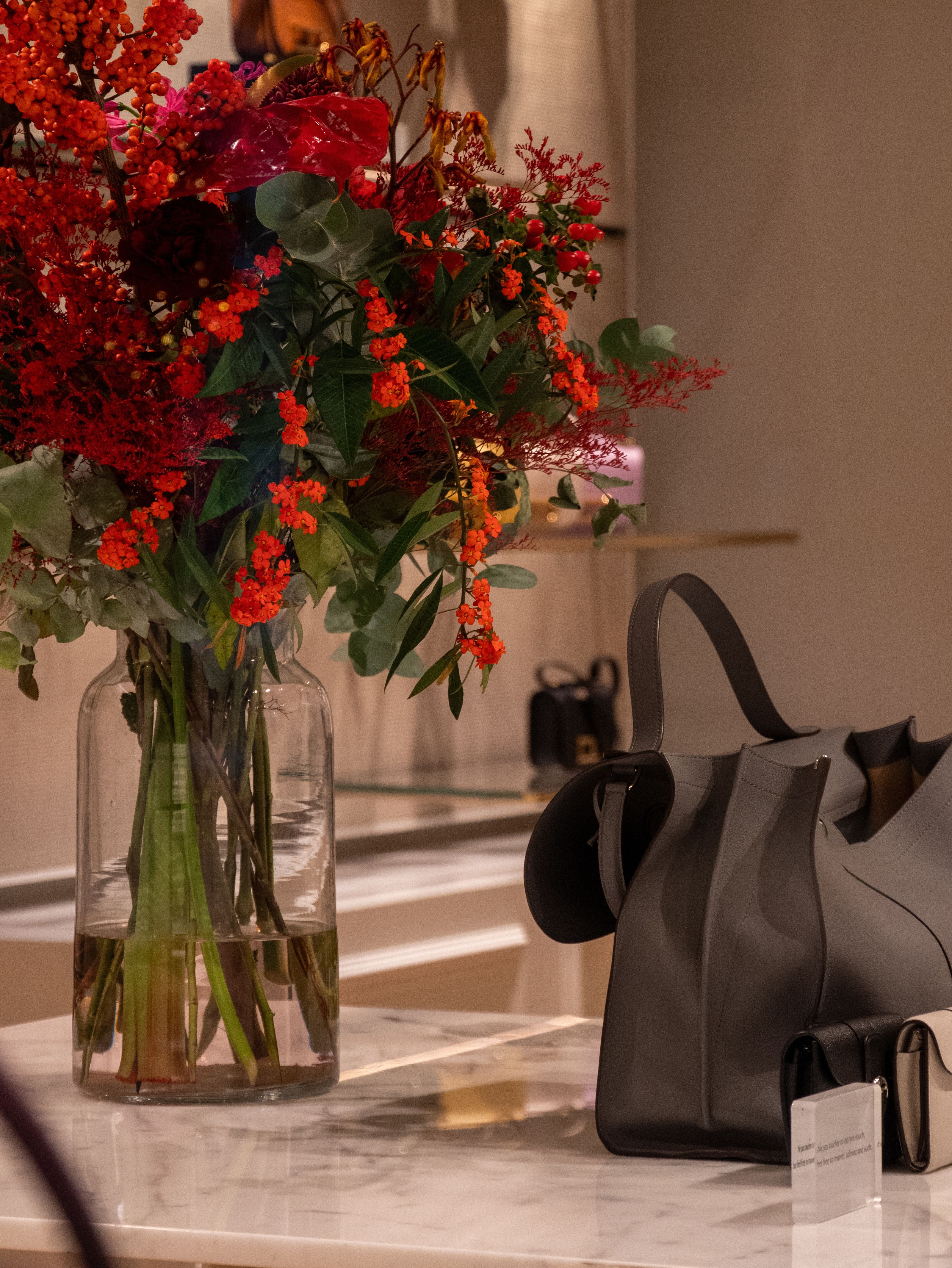 Elegante vitrine de interior com um vibrante buquê e uma sofisticada bolsa de grife sobre uma superfície de mármore.