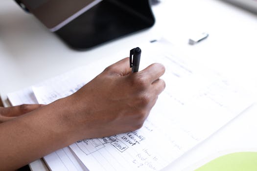 A person writing in a notebook with a pen, focused on planning and notes.