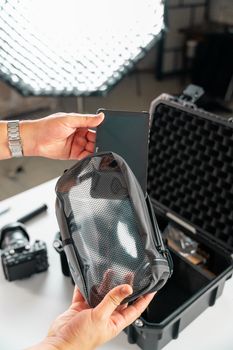 Hands organize camera gear in protective case with tablet and pouch.