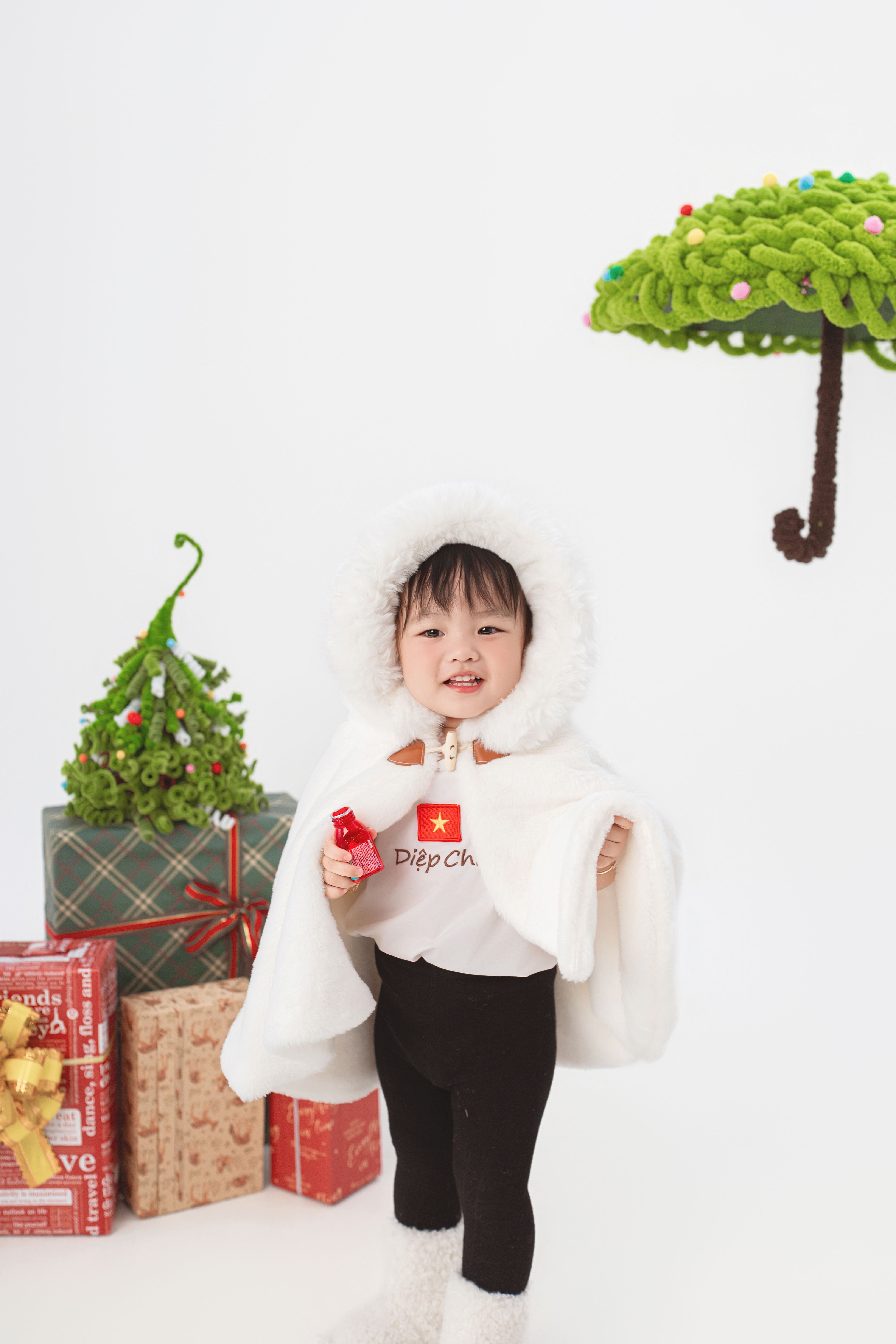 Cute child in winter attire with holiday gifts and decorations, spreading joy.