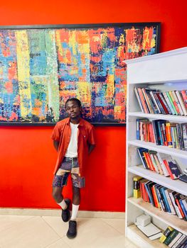 Man with colorful painting and bookshelf, vibrant creative setting.
