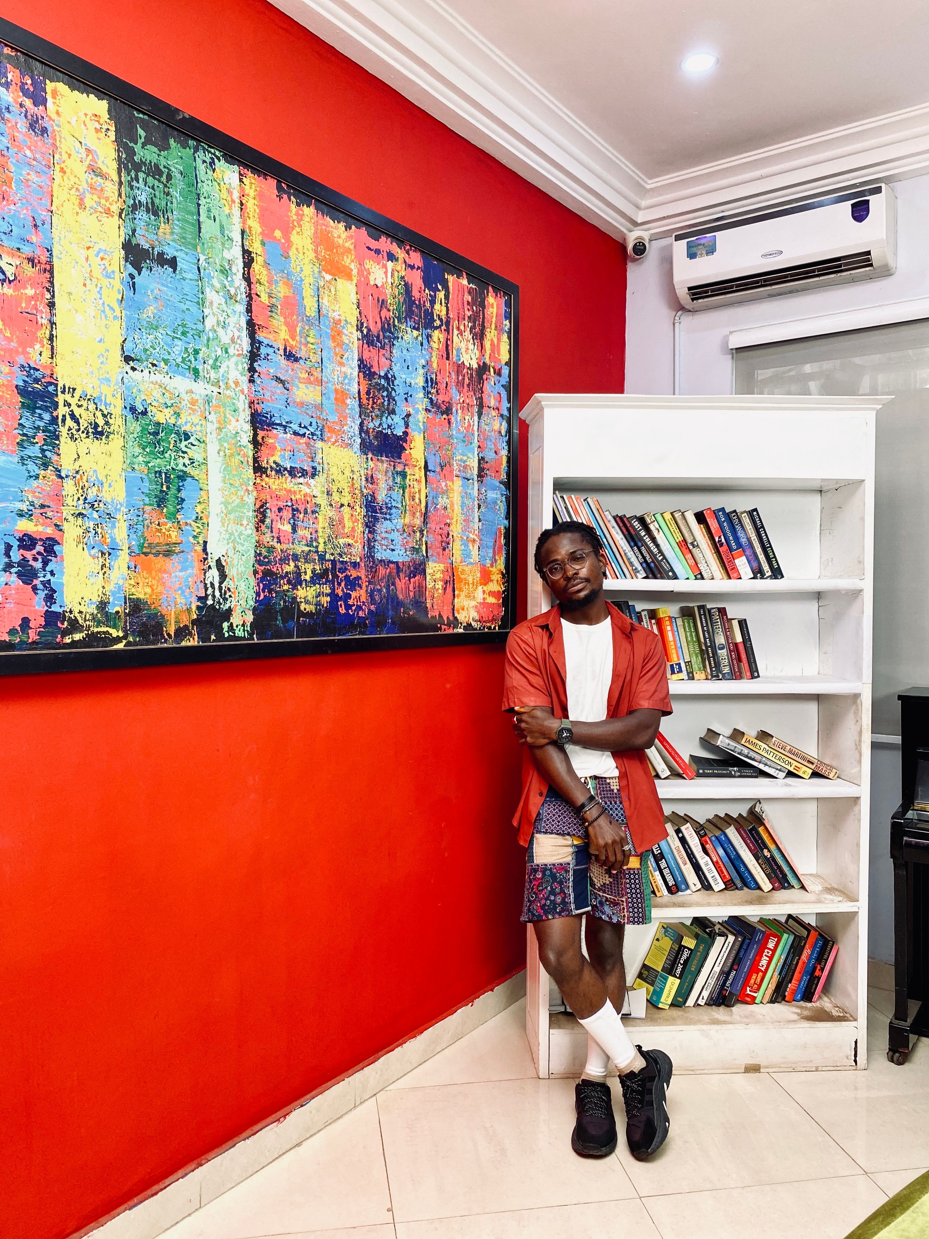A man stands by a bookshelf and abstract painting in a modern, colorful room.