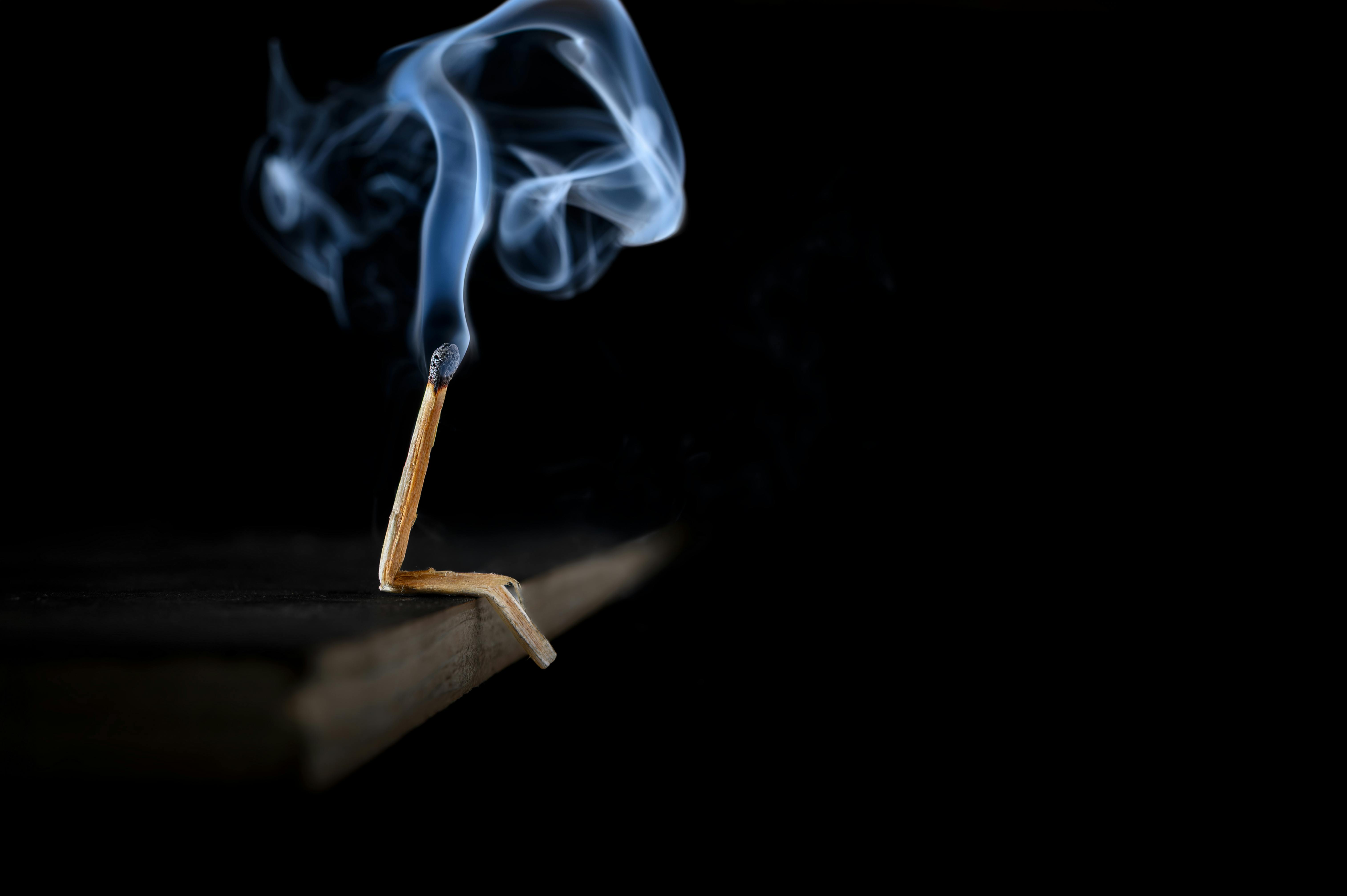 A burnt matchstick with smoke in a dark setting, showcasing minimalist photography.