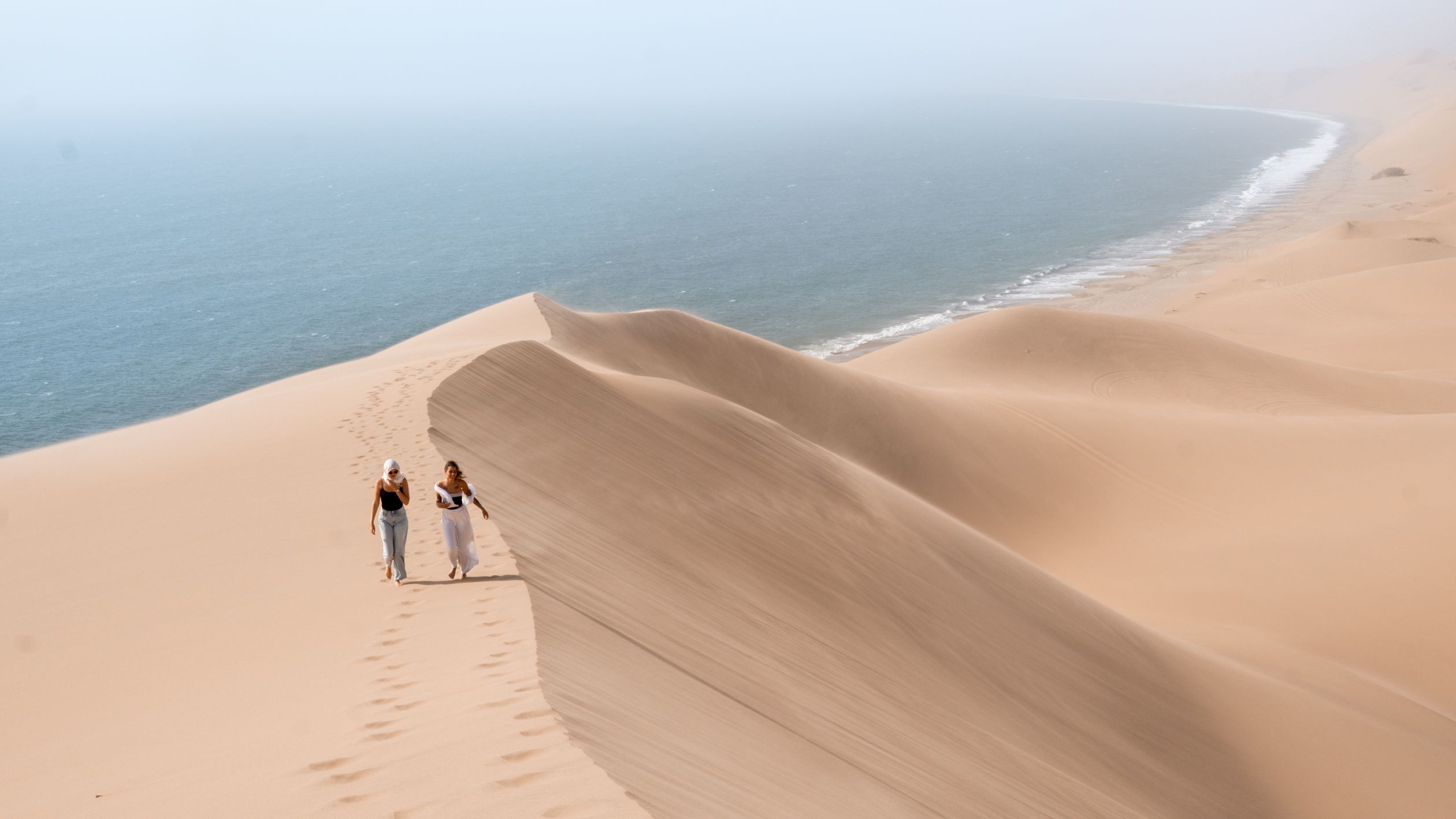 Two women walking on the majestic sand dunes overlooking the Namibian coast.