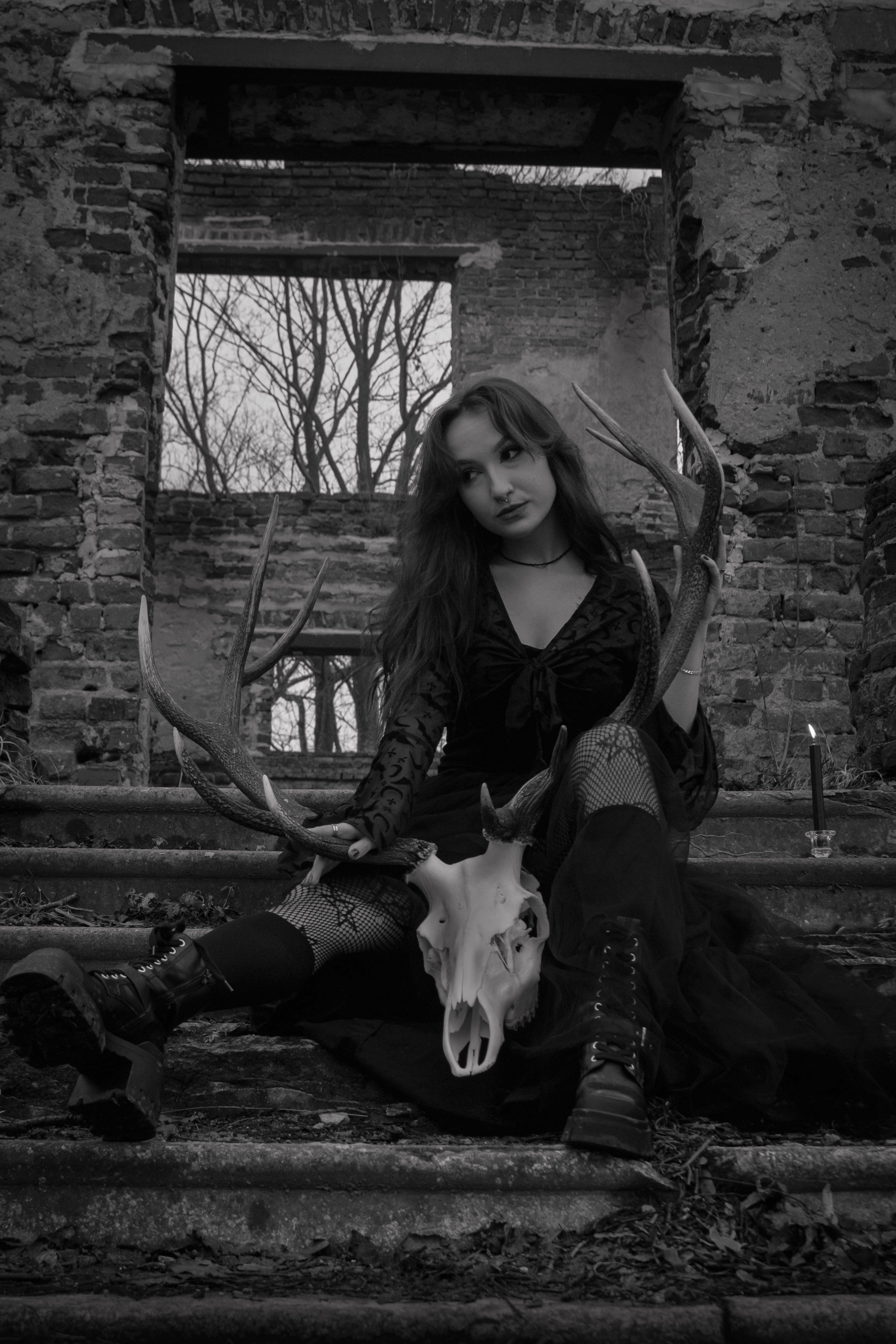 Gothic woman holding antlers in a dramatic, ancient ruins setting.