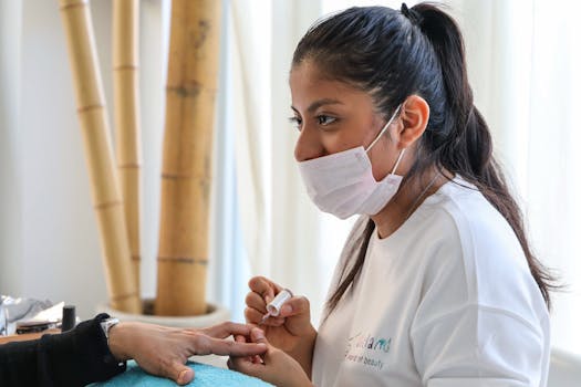 Nail technician wearing a mask, applying polish to a customer's nails in a salon.