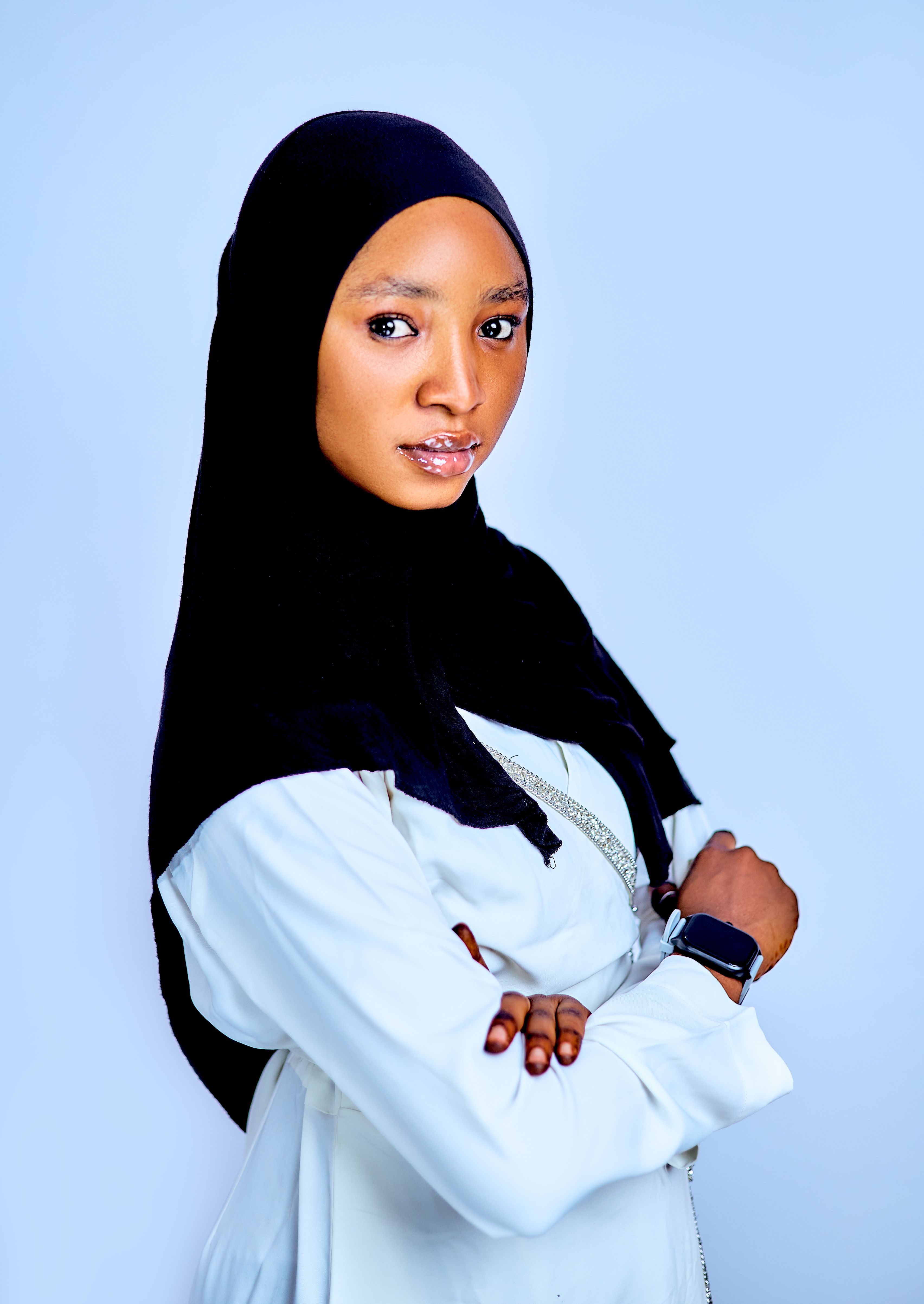 Portrait of a confident woman in a black hijab and white outfit, wearing a smartwatch.