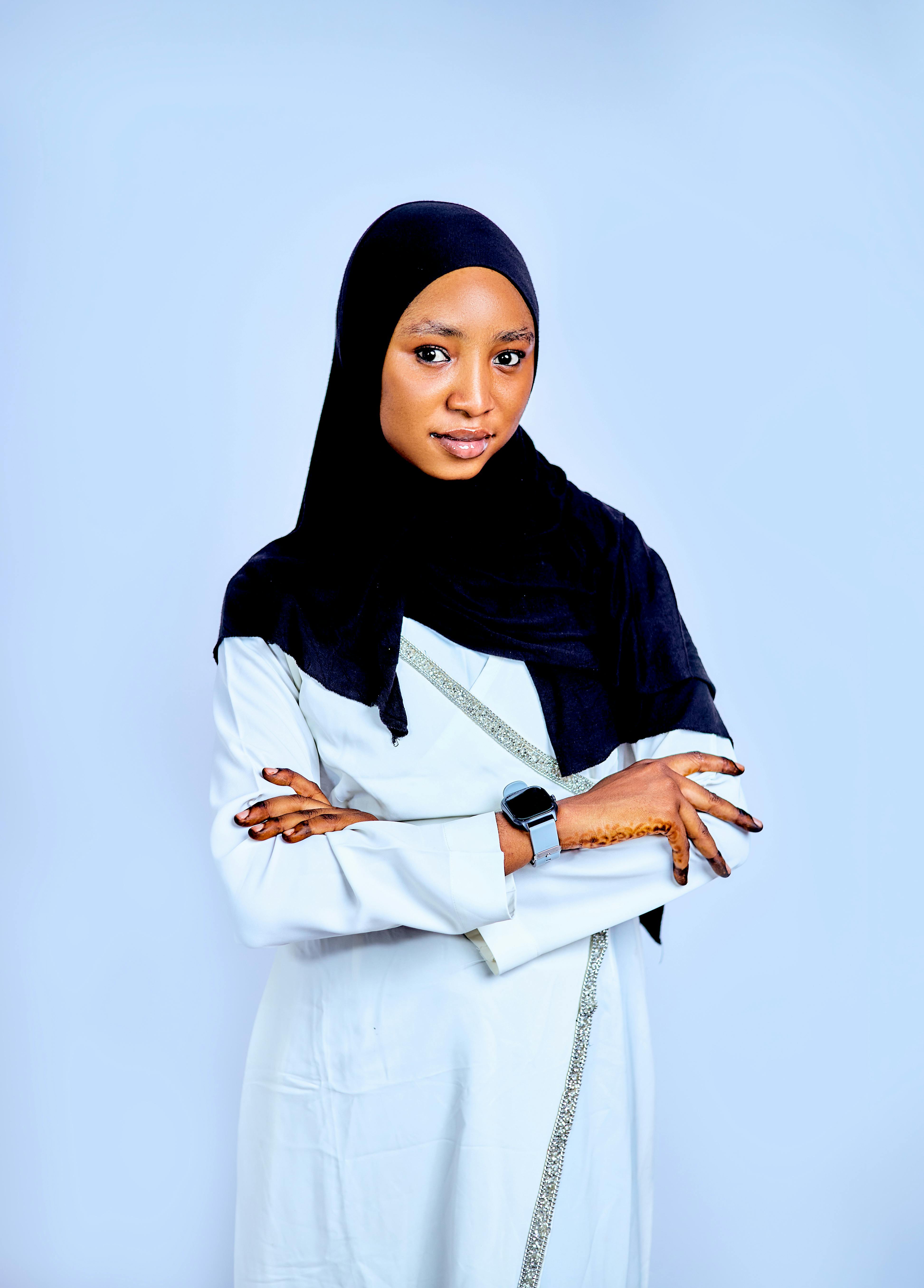 Portrait of a confident Muslim woman wearing traditional attire and a smartwatch against a blue background.