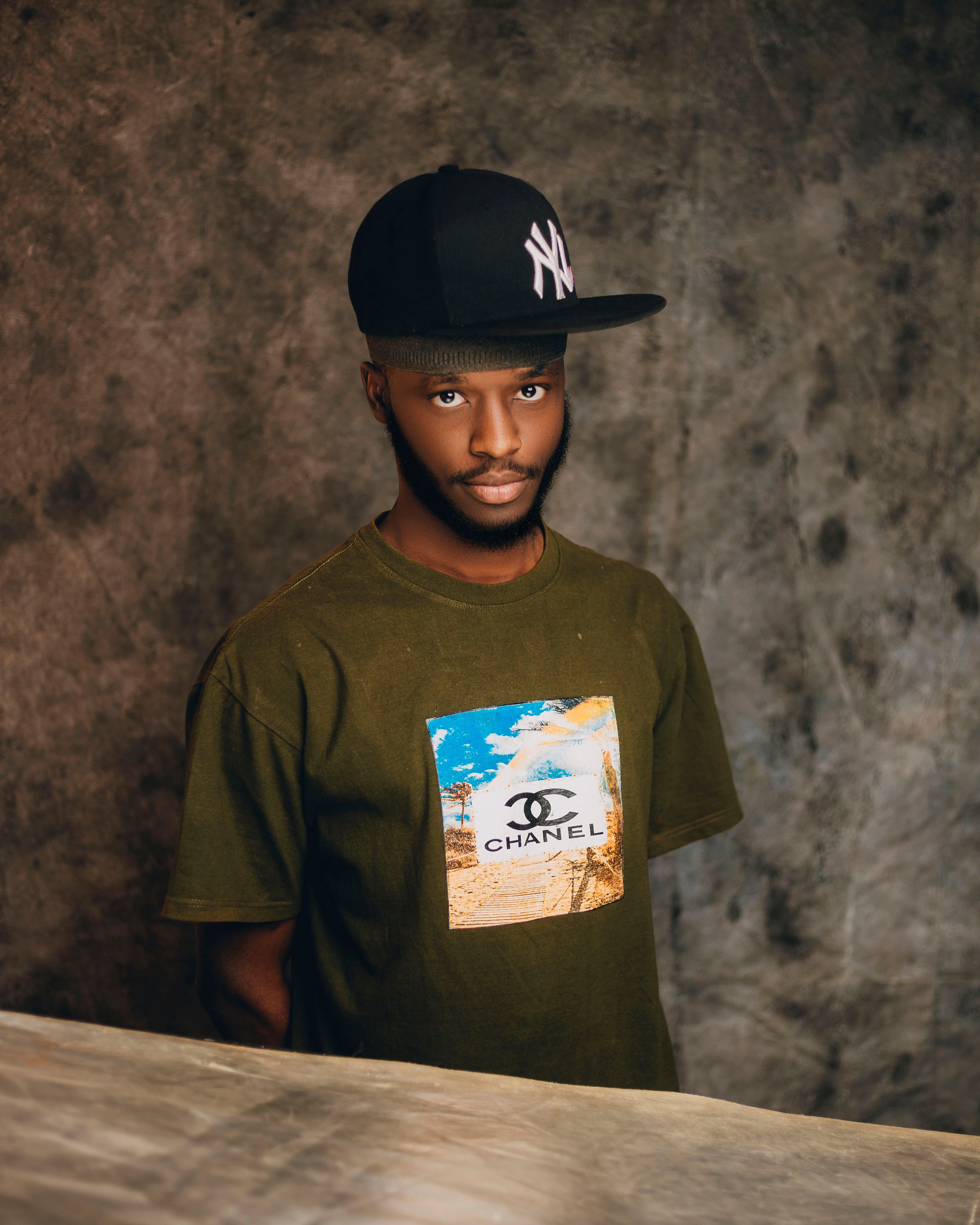 Young man wearing cap and t-shirt, standing against textured backdrop.