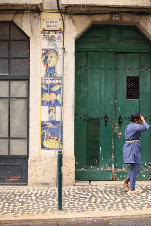 Free A woman walks past an artistic tile facade and green door in Lisbon. Stock Photo