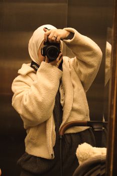 Woman in warm attire takes self-portrait in elevator mirror.