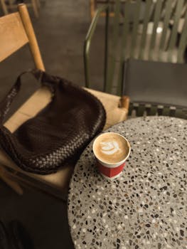 Artistic latte on terrazzo table with wicker bag in cozy cafe setting.