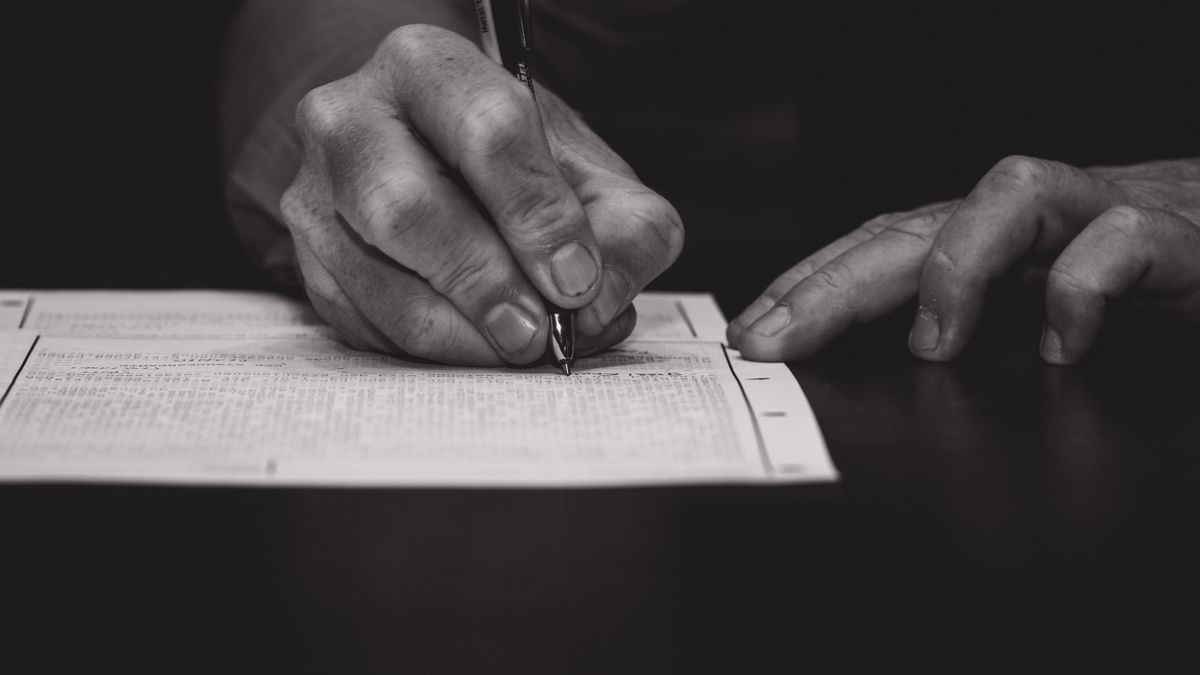 Monochrome image of a hand writing on a document, emphasizing attention to detail.