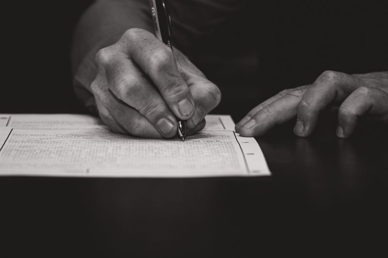 Monochrome image of a hand writing on a document, emphasizing attention to detail.